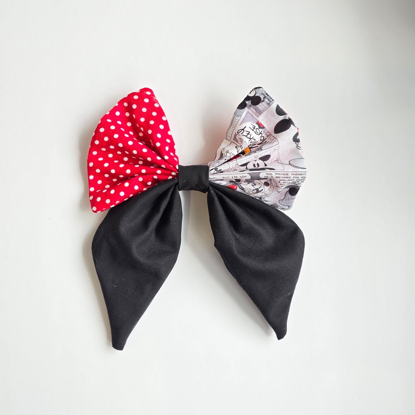 Small black, red polka dot, and character patterned comic style fabric bow on a white background