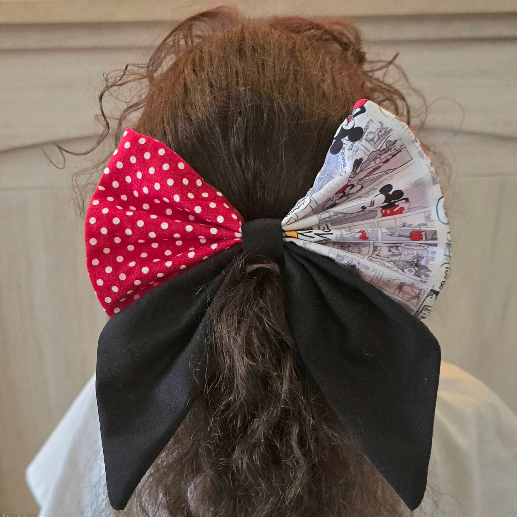 Large handmade patchwork hair bow with red polka dot fabric worn in curly hair