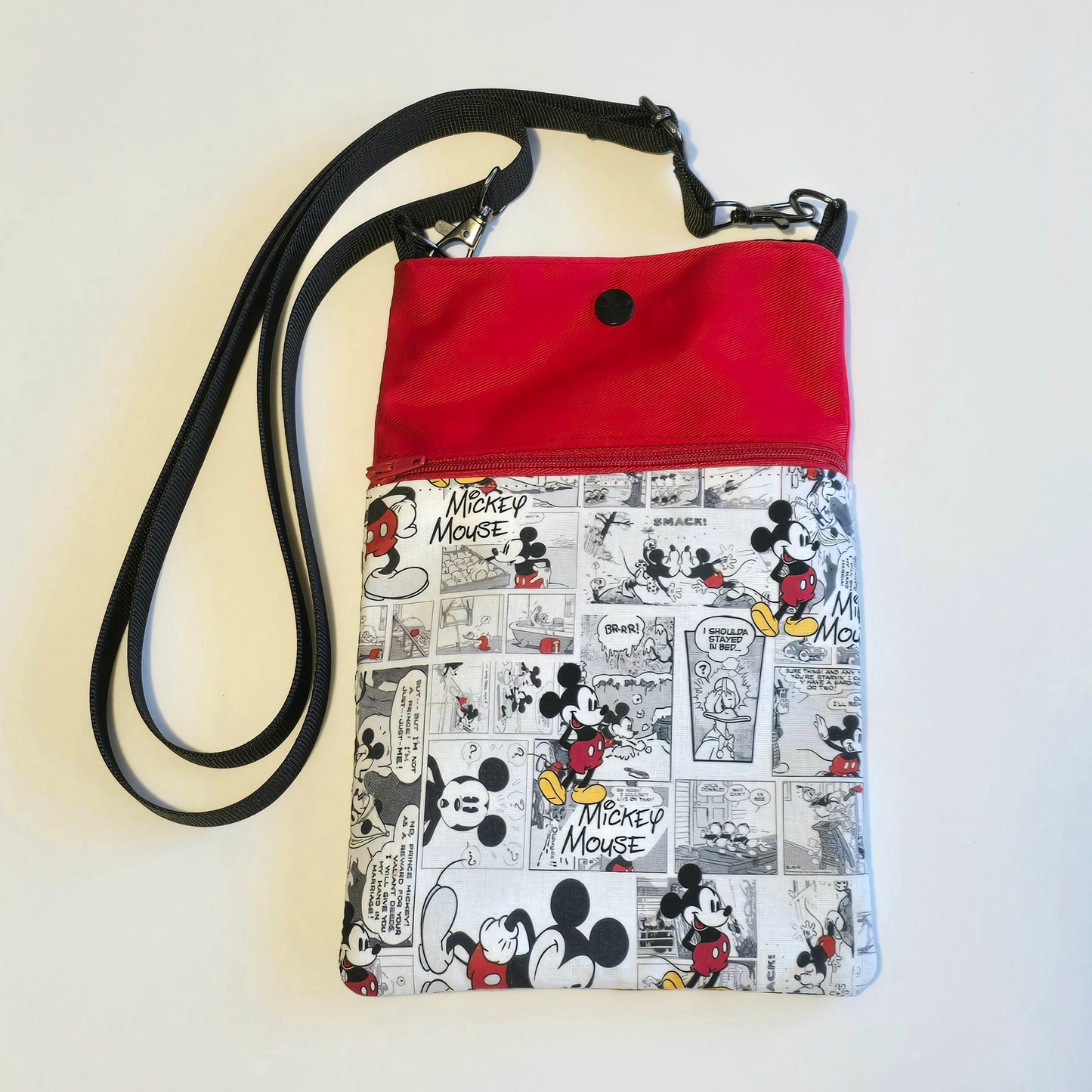 Front view of adjustable crossbody phone bag with comic print fabric and black shoulder strap